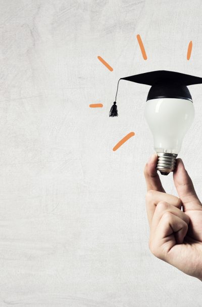 Hand of businessman holding glowing light bulb with graduation hat on it